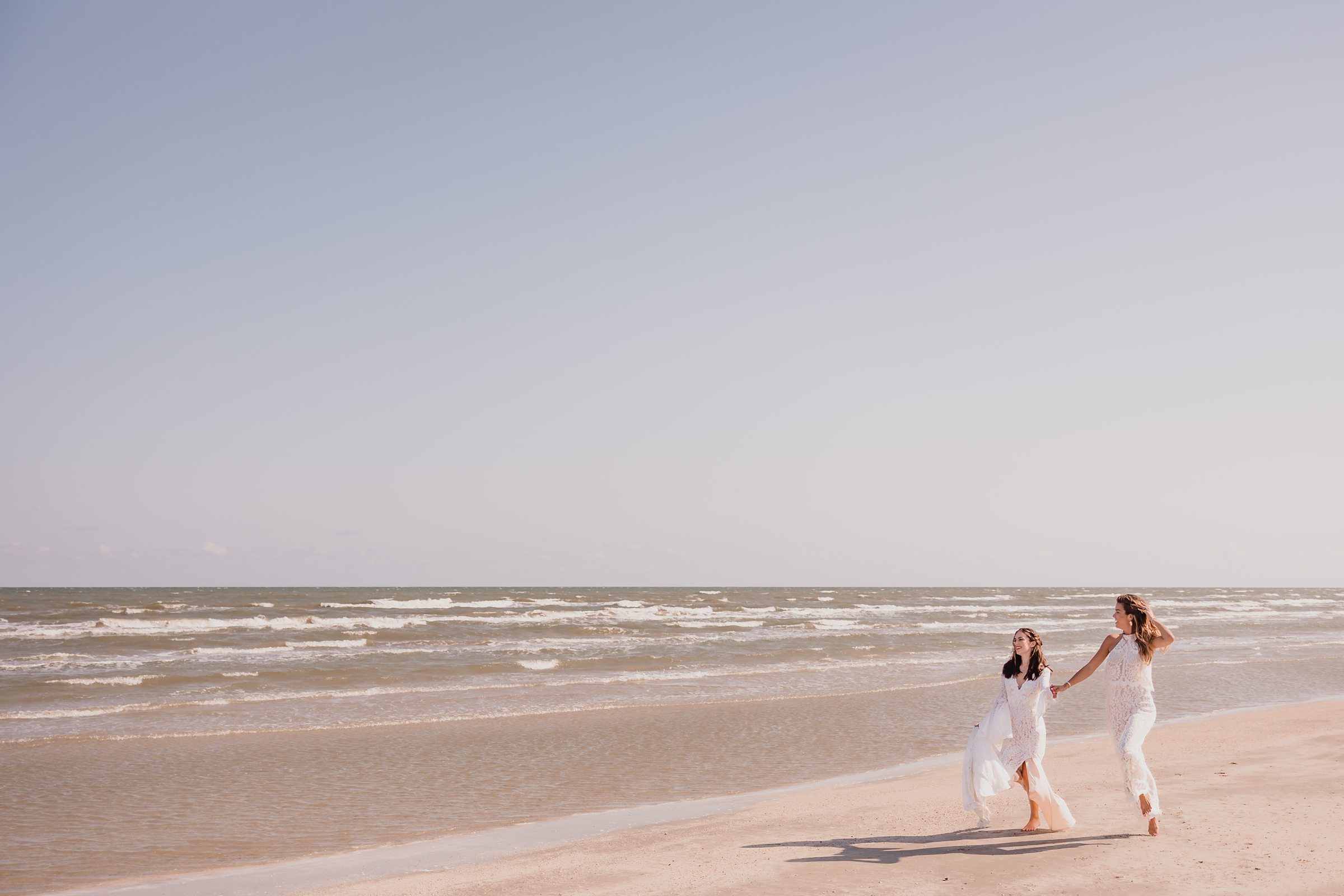 Brides run down the beach during an elopement at Galveston Beach in Texas.