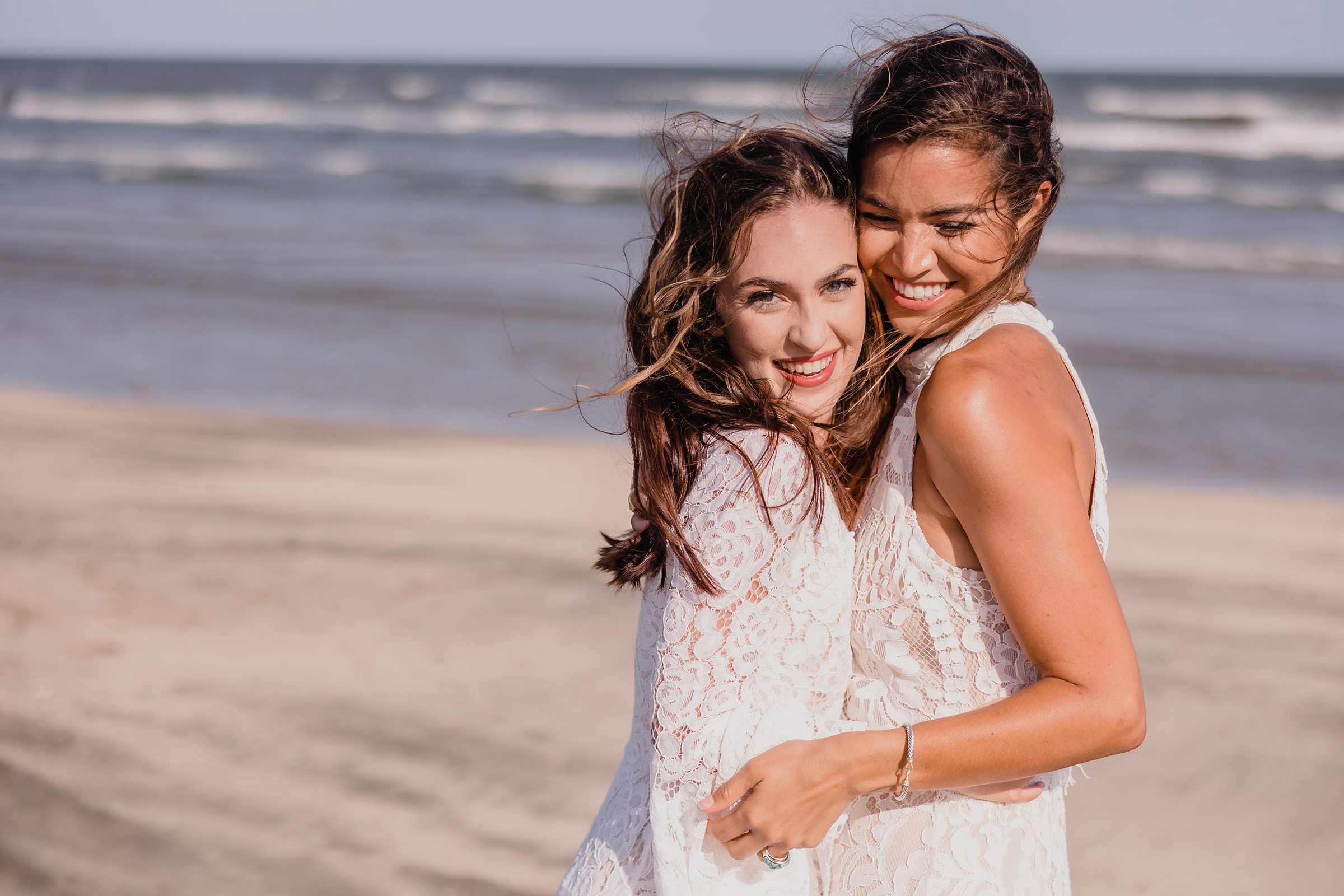 Brides laugh together during an elopement at Galveston Beach in Texas.