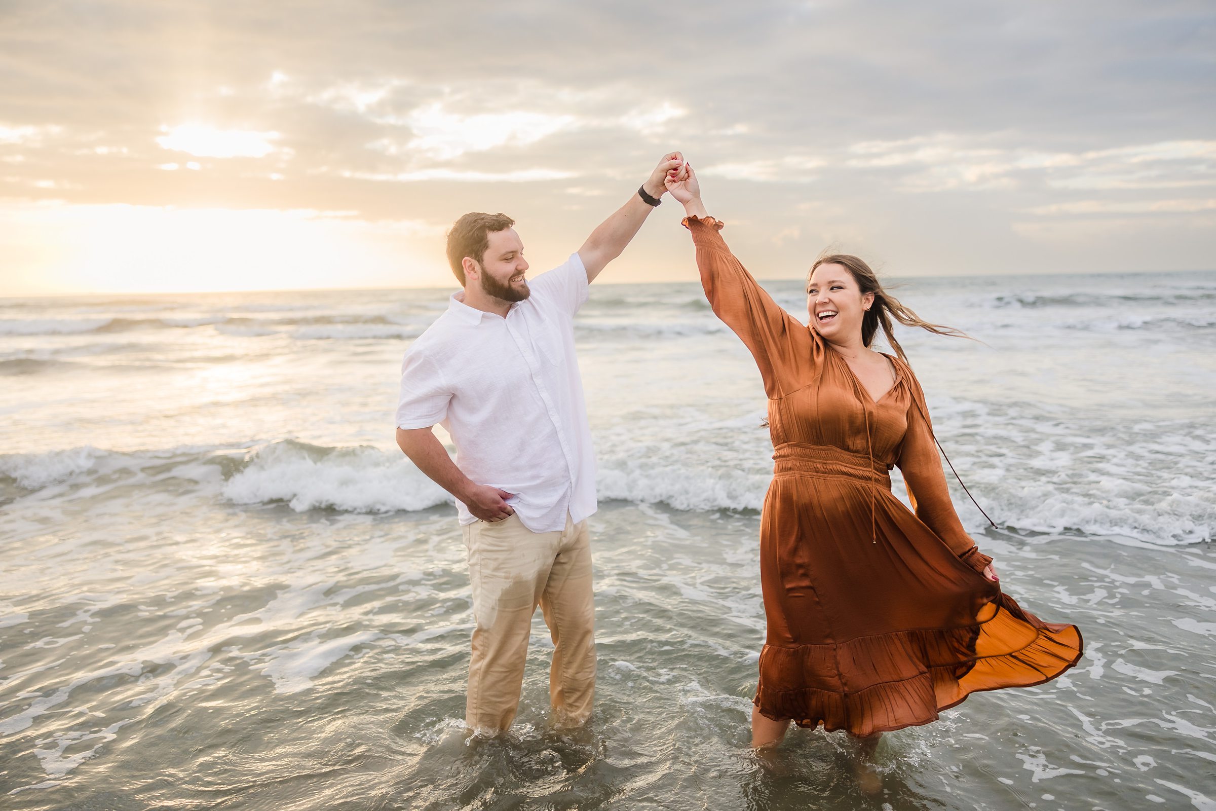 Couple twirl in the ocean during their Galveston Beach engagement session.