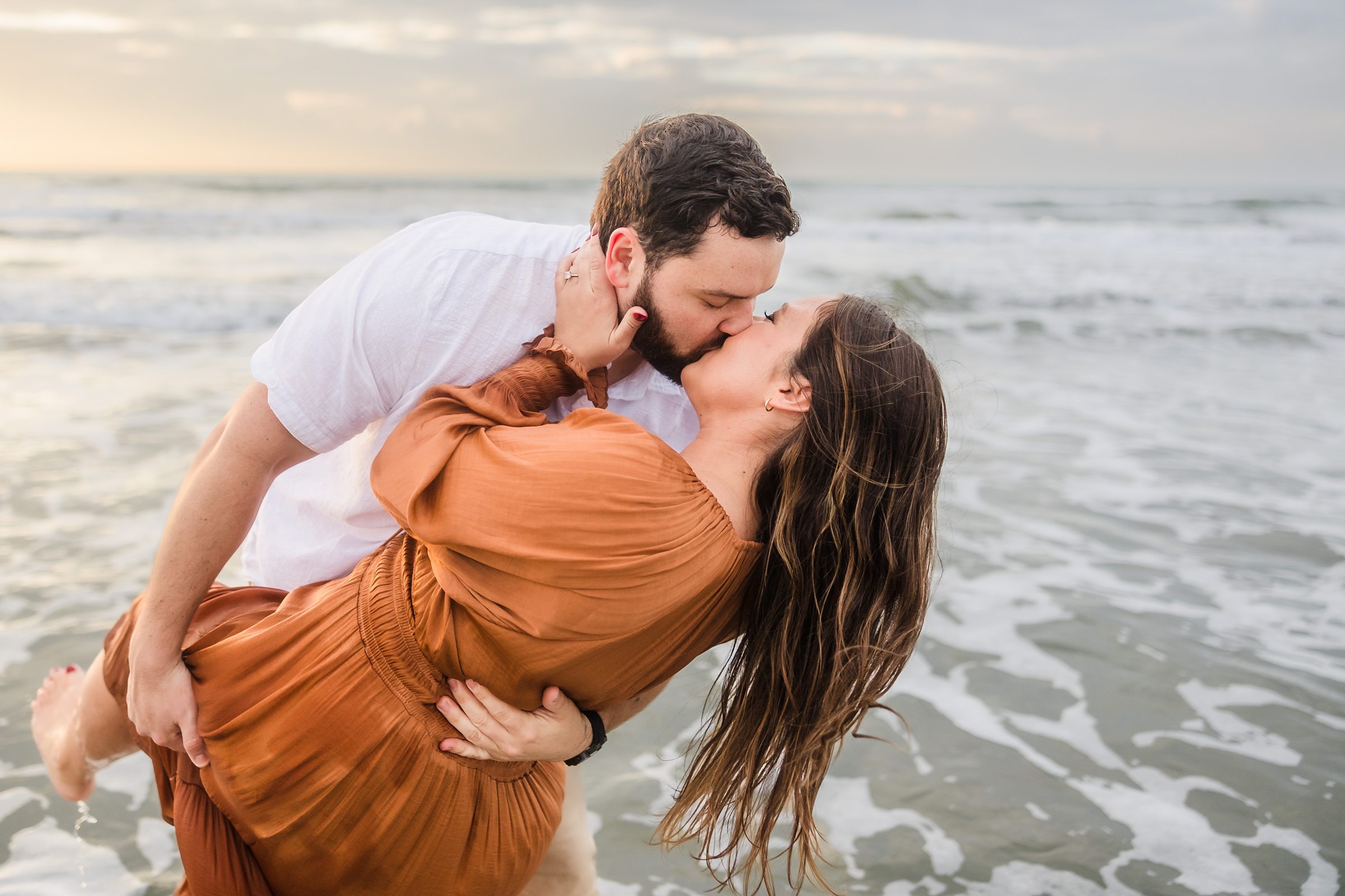 Couple kiss in the ocean during their Galveston Beach engagement session.