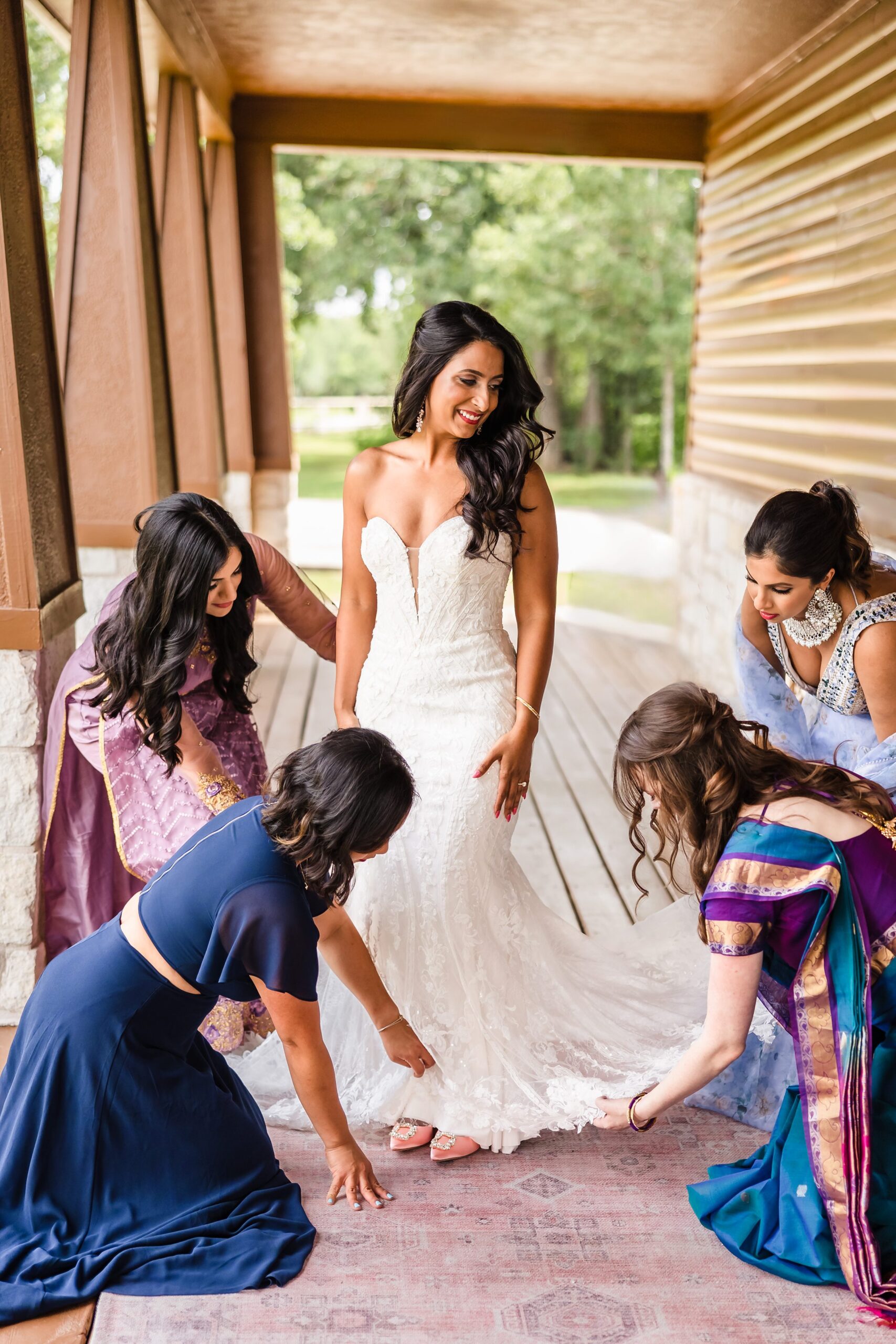 Bridesmaids help bride put on her dress the Shiraz Garden Wedding Venue in Bastrop, Texas.